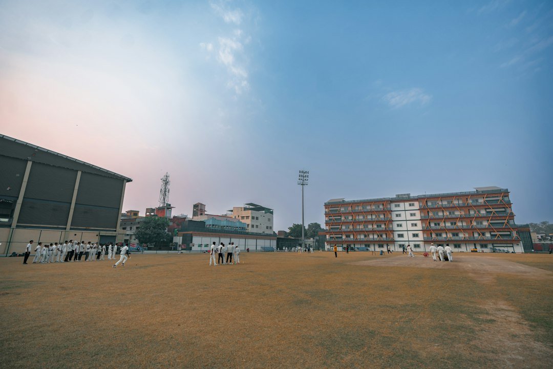 people-playing-cricket-on-a-field-with-buildings-around-7tbrj7jrlqa